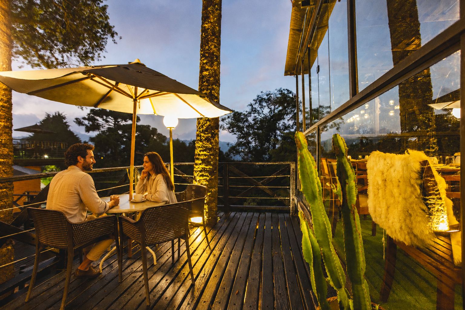Casal no deck do hotel ao entardecer, com vista para as araucárias
