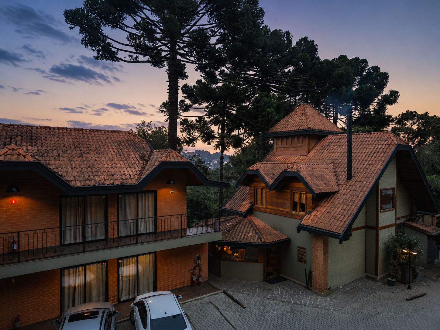 Fachada do DOM Hotel Boutique ao entardecer, entre as araucárias